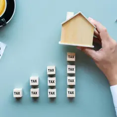 Kto płaci podatek od nieruchomości w spółdzielni mieszkaniowej? Drewniany domek na kostkach z napisem "TAX" symbolizuje koszty.