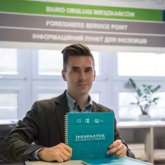 Młody mężczyzna trzyma informator, który może pomóc w kwestii jak sprawdzić zameldowanie. W tle widnieje napis "Foreigners Service Point".