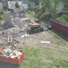 Koparka pracuje przy rozbiórce budynku. Gruz trafia do kontenerów. Oto jak zrobić opis rozbiórki.