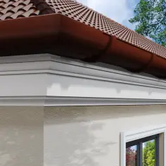 Elegancki biały gzyms na elewacji domu, pod brązową rynną i dachówką.