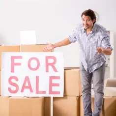 Mężczyzna z kluczami przy kartonach z napisem "FOR SALE" sugeruje, że można sprzedać dom z hipoteką.