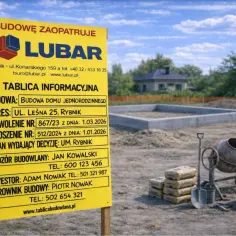 Tablica informacyjna na budowie domu jednorodzinnego. Widoczny fundament, betoniarka i materiały budowlane.