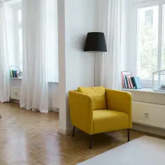 Jasny salon z żółtym fotelem i książkami na parapecie. Zastanawiasz się, ile kosztuje ubezpieczenie mieszkania w bloku?