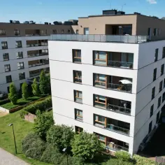 Nowoczesne bloki mieszkalne, zielone tereny i plac zabaw. Widać, że trwa roczny przegląd budynku, wszystko jest zadbane.