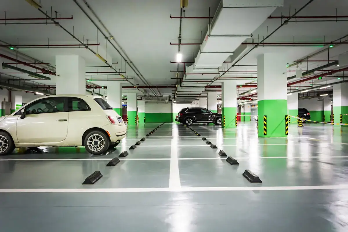 Podziemny parking, gdzie opłaty za garaż we wspólnocie mieszkaniowej są jasno oznaczone. Widać biały i czarny samochód.