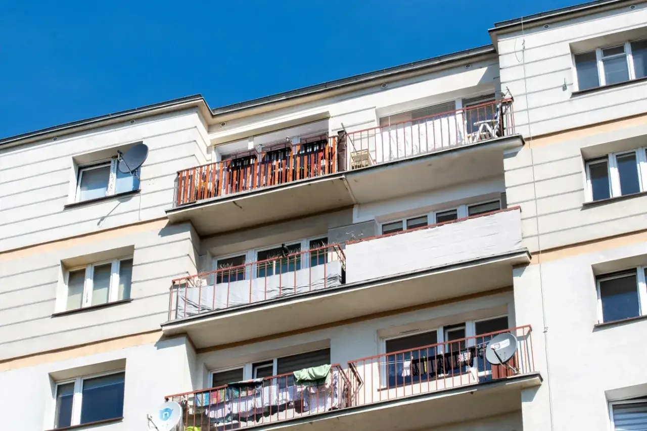 Wielopiętrowy budynek z balkonami, na których suszy się pranie. Czy balkon to część wspólna? Widać anteny satelitarne.