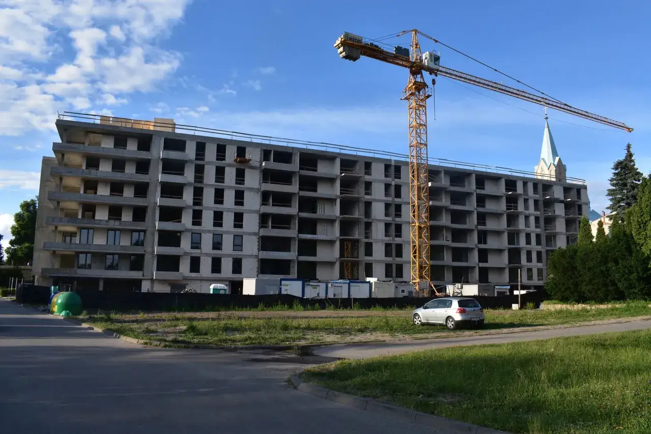 Budowa bloku mieszkalnego, gdzie można dowiedzieć się, jak dostać mieszkanie od spółdzielni. Dźwig budowlany i kościół w tle.